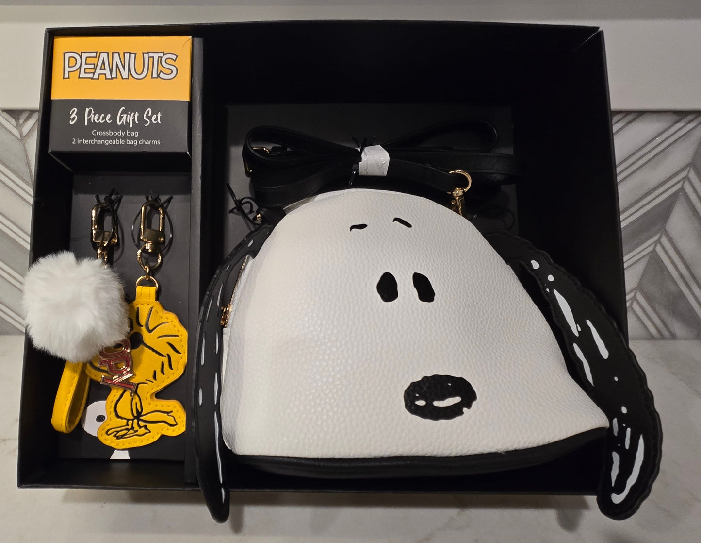 Peanuts-themed keychain and pouch set in a black box on a marble surface.