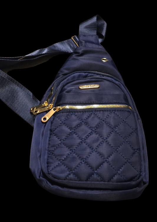 Navy blue quilted sling bag with gold zipper on a beige surface